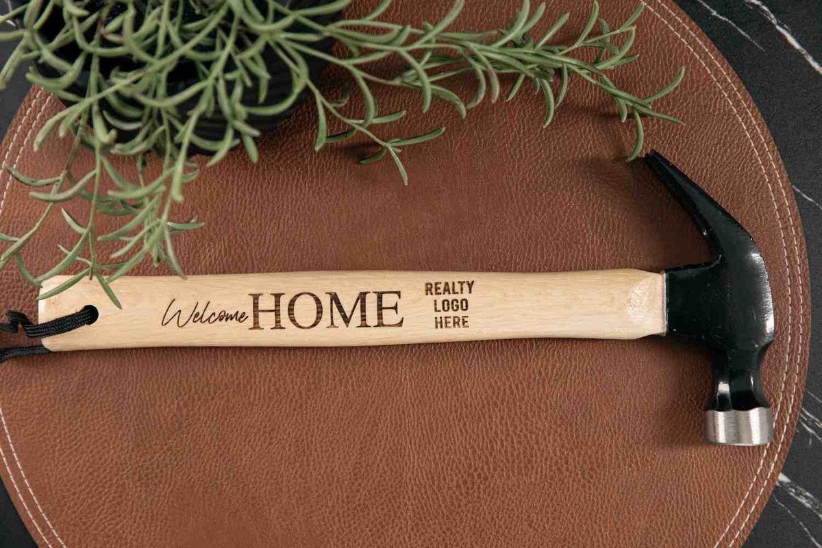Hammer with 'Welcome HOME' engraving on a brown surface with a plant.