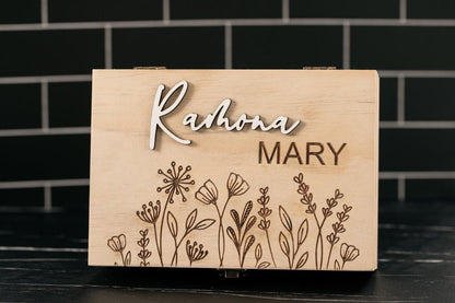 Wooden box with engraved name 'Rahona Mary' and floral design on a black tiled background