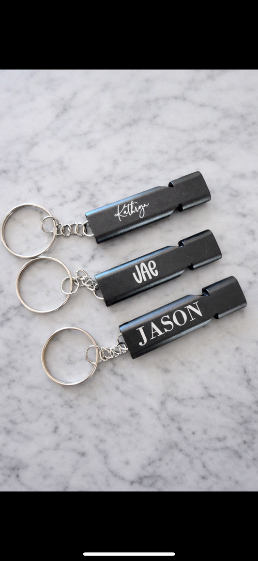 Three black keychains with names engraved on them against a marble background.