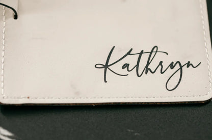 White leather wallet with 'Kathryn' engraved on a dark surface