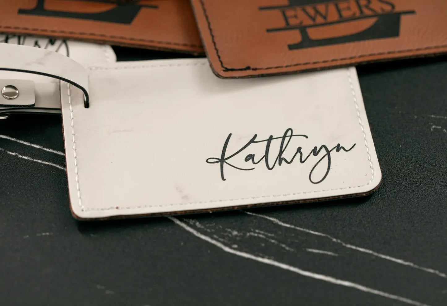 White luggage tag with 'Kathryn' engraved on a dark surface