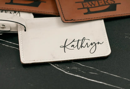 White luggage tag with 'Kathryn' engraved on a dark surface