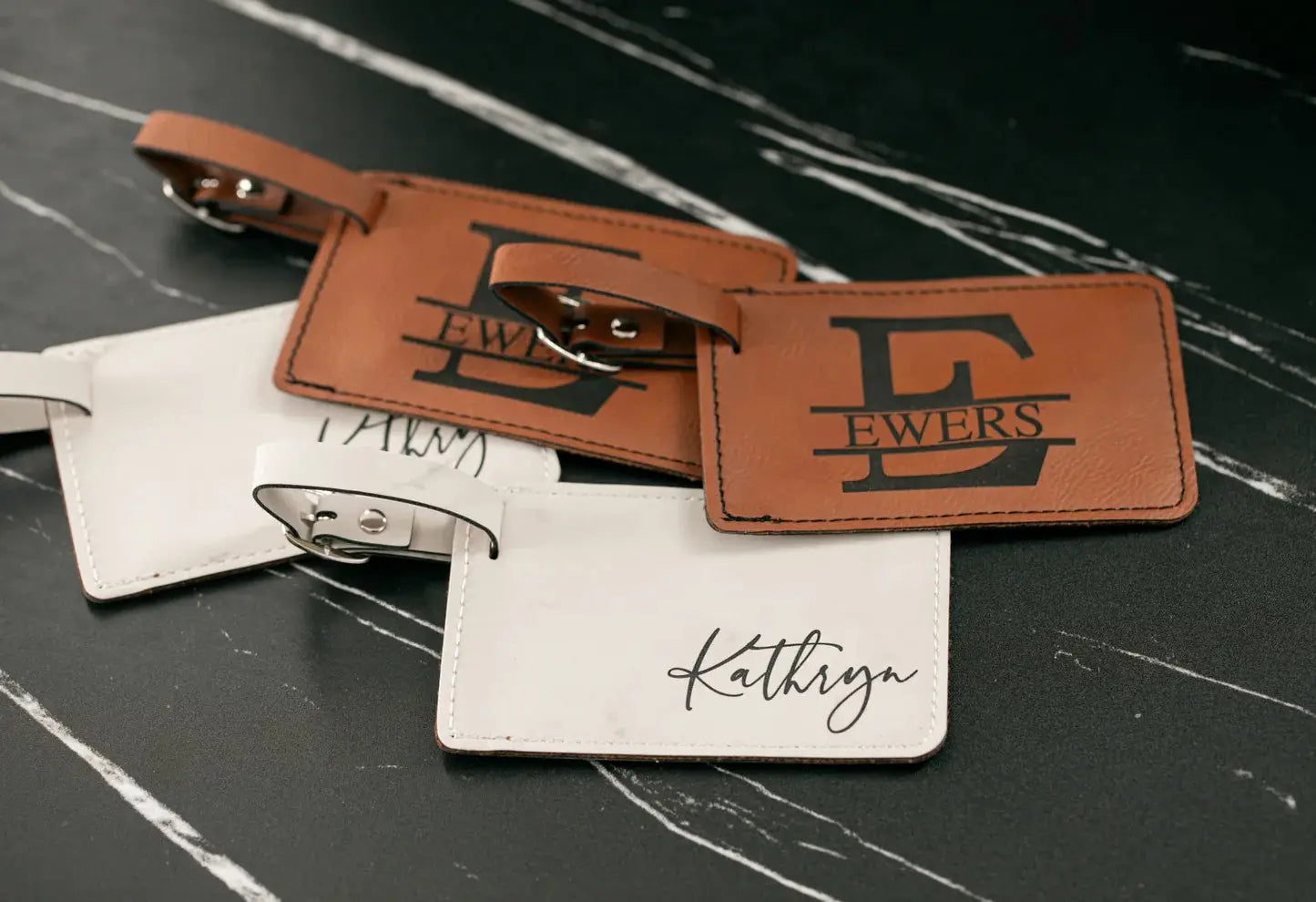 Two luggage tags, one brown with a logo and one white with a name, on a dark surface.