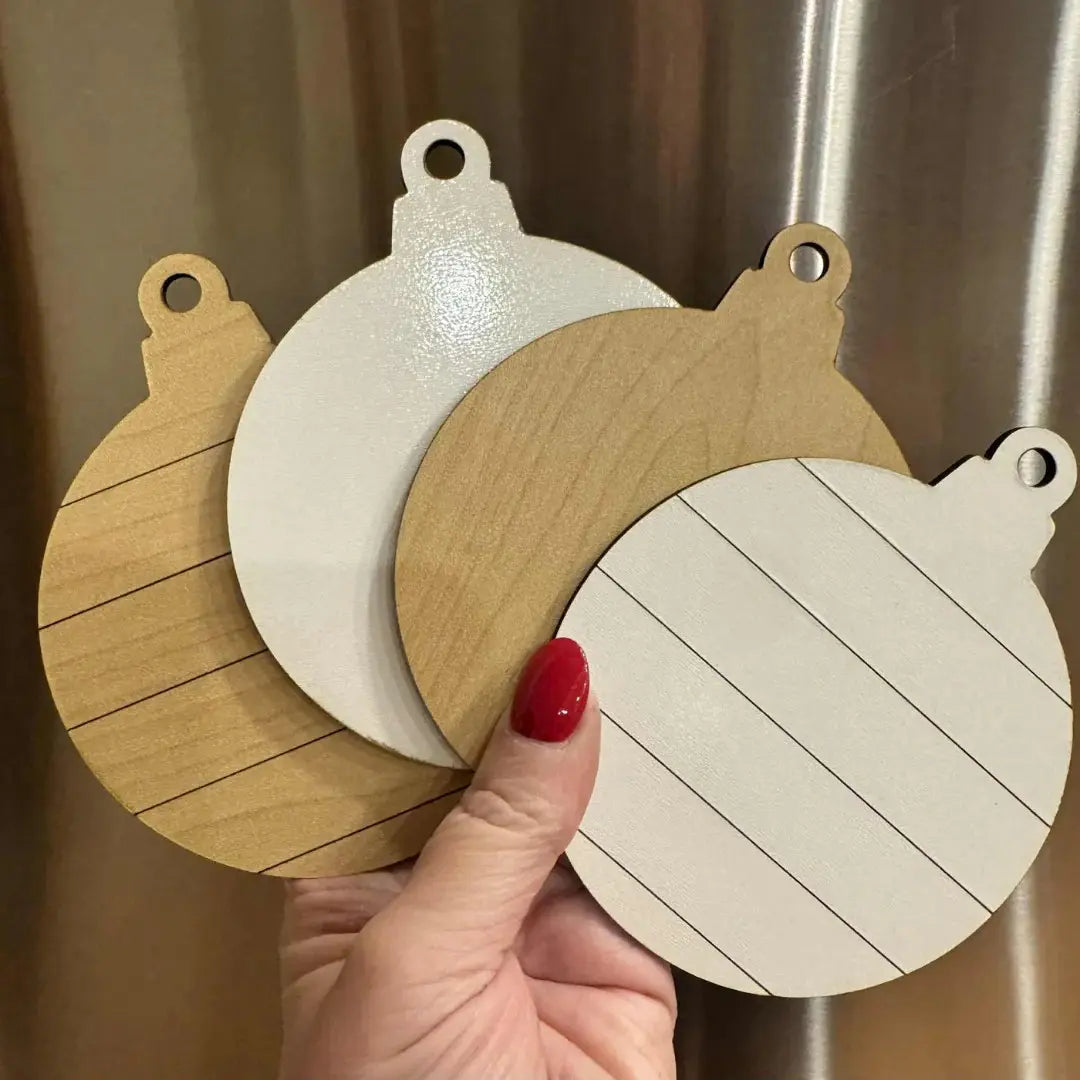 Three wooden coasters with different designs held by a hand against a neutral background