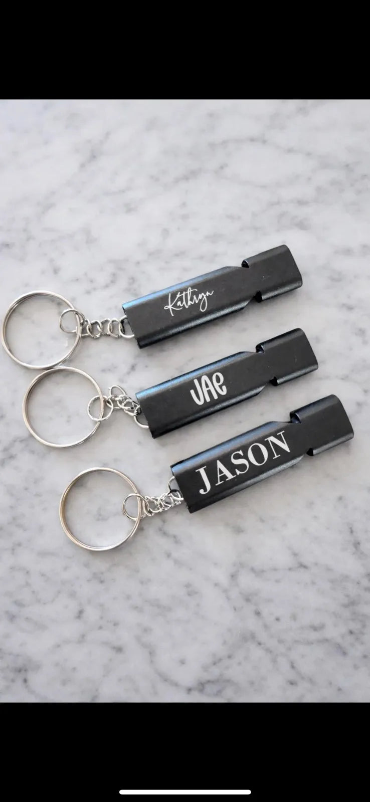 Three black keychains with names engraved on them against a marble background.